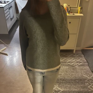 Grön stickad tröja med rund hals - Mysig grön stickad tröja med rund halsringning och långa ärmar. Tröjan har en enkel och stilren design med ribbade muddar vid ärmslut och nederkant. Perfekt för lager-på-lager och chill dagar.