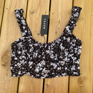 Blommig crop top - Crop top med blommigt mönster från Motel Rocks. Helt oanvänd och har fortfarande taggen på. Den har en och en annan lösa trådar men det är från produktionen, inte pågrund av användning.  Om man vill ha bilder på en modell kan man söka på plaggets namn som står på taggen och hitta bilder på Morel rocks modeller.