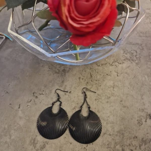 Svarta stora snäckformade örhängen - Säljer ett par svarta örhängen i cool snäckform med räfflad yta. De är stora och hänger snyggt från örat, perfekta för att ge din outfit en edgy touch. Passar dig som gillar statement-smycken och vill sticka ut lite extra.