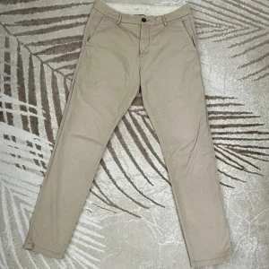 Beige chinos i bomull - Casual slim-fit herrbyxa. Bekväm och fin att ha vid speciella tillfällen eller som en vardagsbyxa.  Storlek M.  Material: 98% bomull, 2% elastan Skick: Byxan har ett par mindre fläktar och är något sliten, men fortfarande i fint skick. (Se bilder för detaljer).