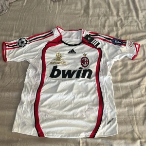 AC Milan Kaka' 22 Champions League tröja - AC Milan fotbollströja från Champions League-finalen 2007 med Kaka' och nummer 22 på ryggen. Vit med röda och svarta detaljer, Adidas ClimaCool-material och broderade märken. Klassisk design med korta ärmar och officiella patches på ärmarna.