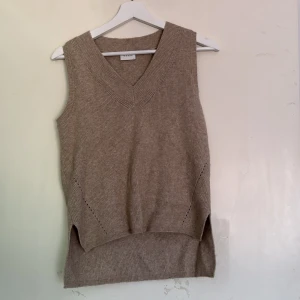 Beige stickad väst från Vila - Stickad beige väst från Vila i storlek XS. Västen har v-ringad hals, ribbad struktur och slitsar i sidorna för en chill och avslappnad look. Perfekt att slänga över en skjorta eller t-shirt för extra lager.