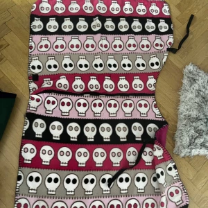 länn täcke häst - Cool länn täcke med färgglada döskallar i rader på rosa, svart och beige bakgrund. Täcket har knytband i sidan och är fodrad med cerise fleece på insidan. Perfekt för dig som vill sticka ut med en unik och lekfull stil. Storlek häst