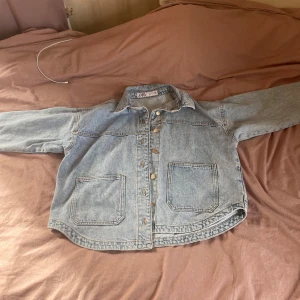 Ljusblå jeansjacka från Zara - Säljer en ljusblå jeansjacka från Zara i storlek S. Jackan har klassisk krage, två stora fickor framtill och knäppning med slilvriga knappar.. Aldrig använt säljer då den är för stor för mig…