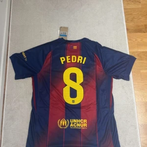 FC Barcelona Pedri #8 matchtröja Nike - Säljer en officiell FC Barcelona matchtröja med Pedri #8 på ryggen. Tröjan är blå och röd med gula detaljer, klubbmärke och sponsorer på bröstet. Tillverkad i lätt och ventilerande polyester, perfekt för fotboll eller att bära som supporter. Perfekt för dem som älskar fotboll!! Priset kan diskuteras. Aldrig använt förut. Anledning till att jag säljer tröjan är eftersom den inte passar mig.