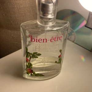 Bien-Être L'Herboriste parfym - Fräsch cologne från Bien-Être, L'Herboriste-serien. Flaskan är genomskinlig med blommiga detaljer och text i rosa och vitt. Doften har örtiga och blommiga inslag, perfekt för dig som gillar naturliga och lätta parfymer.