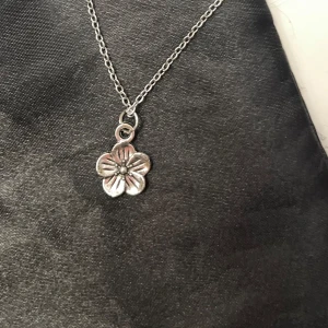 Blomma choker silver imitation halsband blomma - En blomma trädd på en kortare kedja i silverimitation som är justerbar 35-40 cm. Berlocken är ca 1 x 1 cm. 