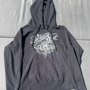 Parkway Drive svart hoodie med tryck - Svart hoodie från Parkway Drive med stort tryck fram och bak. Framsidan har bandets logga och ormmotiv, baksidan har dödskalle, ormar och texten 'Crushed'. Klassisk känguruficka, huva med snörning och långa ärmar. Perfekt för dig som gillar metal och streetstyle. Väldigt liten i storlek, passar bättre M