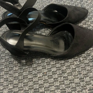Svarta pumps med spetsig tå och klack - Svarta pumps med spetsig tå och låg klack. Skorna har en elegant rem över foten och är tillverkade i mocka-liknande material. Perfekta för dig som gillar stilrena och klassiska skor med en modern twist.strlk41 men passsar väldigt bra med 40!🩷