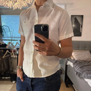 Vit kortärmad linneskjorta Dressmann - Fräsch vit kortärmad skjorta från Dressmann i linnemix. Klassisk krage, knappstängning och bröstficka med knapp. Perfekt till jeans eller shorts för en clean och stilren look. Skön och luftig känsla tack vare linnematerialet.