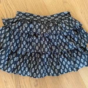 Svart volangkjol med mönster - Supersöt svart kortkjol med flera volanger. Lätt och luftig. Aldrig använd.