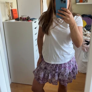 Lila volangkjol   - Kort volangkjol från Revelation i lila och vita toner med mönster. Kjolen har smock i midjan och dubbla volanger nertill. 