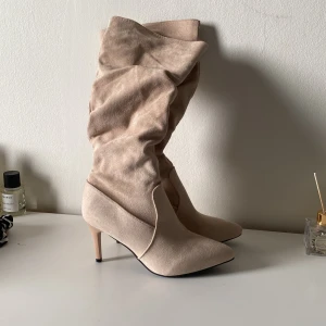 Beiga mockastövlar med klack - Snygga beiga (kaki) stövlar i mocka med spetsig tå och smal klack. Aldrig använda!