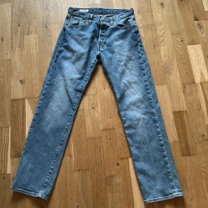 Levi's 501 ljusblå jeans W26 L28 - Klassiska Levi's 501 jeans i ljusblå denim med raka ben och normal passform. Byxorna har fem fickor, knappgylf och ikonisk läderpatch bak i midjan. Aldrig använda.  Djur och rökfritt hem.