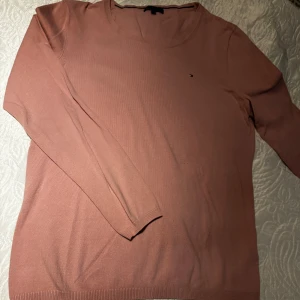 Rosa stickad tröja Tommy Hilfiger L - Snygg rosa stickad tröja från Tommy Hilfiger i storlek L. Klassisk rund halsringning och diskret logga på bröstet. Perfekt för dig som gillar stilrena och bekväma plagg med en soft vibe. Passar lika bra till jeans som till kjol.