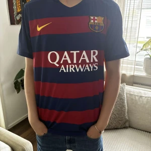 FC Barcelona Messi 10 matchtröja Nike - Säljer en officiell FC Barcelona fotbollströja från Nike med Messi 10 på ryggen. Tröjan har breda blå och röda ränder, gula detaljer och klubbmärke på bröstet. Qatar Airways tryck på framsidan och Champions League-patchar på ärmarna. Materialet är lätt och andas.