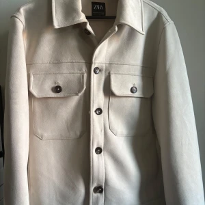 Beige overshirt  - Stilren beige overshirt från Zara med klassisk krage och två stora bröstfickor med knappar. Jackan har en rak passform och är tillverkad i ett mjukt material som ger en clean och modern vibe. Perfekt att slänga över en hoodie eller t-shirt.