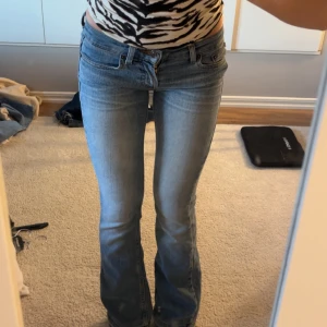 Bootcut ljusblå jeans - Snygga ljusblå bootcut jeans med klassisk femficksdesign och låg midja. Jeansen har en lätt tvättad look och är tillverkade i mjukt denimtyg som sitter skönt på kroppen. Perfekta för dig som gillar en avslappnad men trendig stil. Från American Eagle