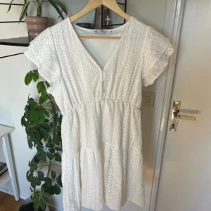 Vit spetsklänning från ONLY - Endast använd 1 gång, nypris 599 kr. Superfin vit kortklänning från ONLY med v-ringning, knappar framtill och vackra spetsdetaljer. Klänningen har korta ärmar med volang och markerad midja. Perfekt för sommarens alla tillfällen och ger en romantisk vibe.