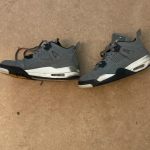 Grå Nike Air Jordan 4 sneakers - Säljer ett par grå Nike Air Jordan 4 sneakers med klassisk meshpanel, svarta och vita detaljer samt Jumpman-logga på hälen. Skorna har snörning, hög siluett och en robust sula med synlig Air-enhet. Perfekta för dig som gillar streetwear och ikoniska basketskor.