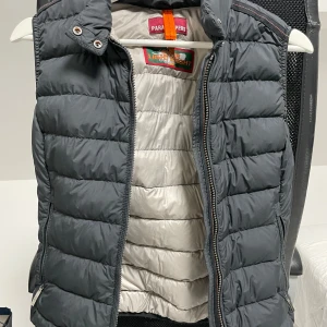 Svart dunväst från Parajumpers - Säljer en snygg och lätt grå dunväst från Parajumpers i storlek XS. Västen har en dragkedja framtill och är perfekt för höst och vår. Den är i mycket bra skick och har en stilren design som passar till det mesta. Perfekt för lager-på-lager-stil! 🍁🍂💨 