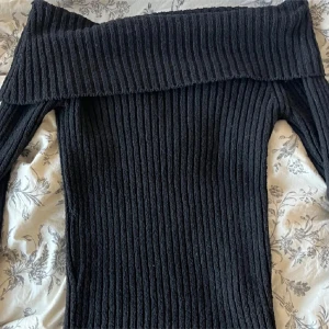 Svart ribbad offshoulder klänning - Säljer en svart ribbstickad tröja med offshoulder-modell och långa ärmar. Tröjan är tight och har en bred, vikt kant upptill som ger en snygg detalj. Perfekt för dig som gillar en stilren och trendig look.
