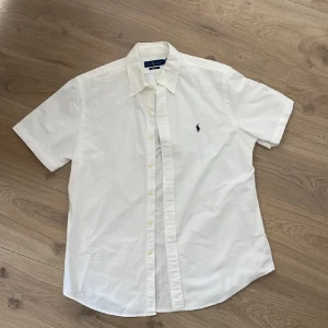 Vit kortärmad skjorta Ralph Lauren - Vit kortärmad skjorta från Ralph Lauren med klassisk krage och knappar framtill. Custom fit-modell med broderad logga på bröstet. Skjortan är i bomull och har en stilren och tidlös look som passar till många outfits.