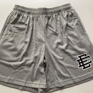 Grå mesh shorts med tryck - Snygga grå mesh shorts med elastisk midja och svart-vitt tryck på ena benet. Perfekta för träning eller chill, med luftig känsla och sportig look. Shortsen har en avslappnad passform och är tillverkade i syntetmaterial för extra komfort.