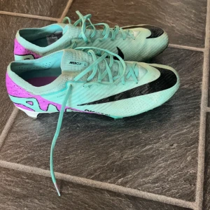Nike Mercurial Air Zoom fotbollsskor - Snygga Nike Mercurial Air Zoom fotbollsskor i ljus turkos med svarta detaljer och lila häl. Skorna har snörning, platt sula med dobbar och är tillverkade i syntetmaterial för bästa grepp och känsla på planen. Perfekta för dig som vill sticka ut på matchen.  Säljer pågrund av för små för mig använda väldigt sällan, inga hål eller några skador behöver bara putsas lite 👍🏽