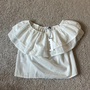 Vit offshoulder top Meet Me There - Supersöt vit offshoulder blus från Meet Me There med bred volang runt hela axelpartiet. Tunn och luftig, perfekt för sommaren!! Den går att ha runt båda armar och endast en vilket är mkt trendigt. Passar mer S skulle jag säga eftersom den är ganska kort och mindre i storleken. Inte använd.