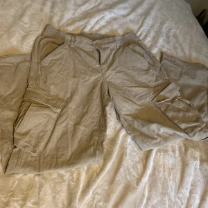 Beiga cargobyxor i manchester - Säljer ett par beiga cargobyxor i mjuk manchester med elastisk midja och stora fickor på sidorna. Byxorna har en relaxed fit och är perfekta för en chill och avslappnad stil. Passar dig som gillar praktiska detaljer och skön känsla.
