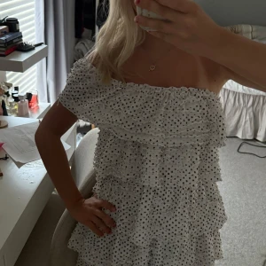 Vit prickig offshoulder volangklänning - Supersöt kort offshoulder-klänning i vitt med svarta prickar och flera volanglager. Klänningen har en luftig passform och är perfekt för varma dagar. Den är ärmlös och har en romantisk vibe med sina volanger och prickiga mönster. Från Zara, använd några gånger men i bra skick, man kan ha klänningen på flera sätt