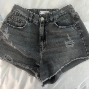 Grå midwaist jeansshorts med slitningar - Snygga grå jeansshorts från Zara med slitna detaljer och råa kanter. Klassisk femficksmodell med knapp och dragkedja framtill.