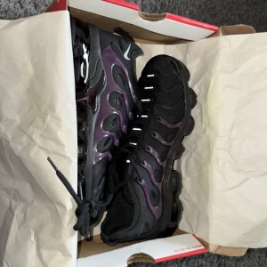 Nike Air Vapormax Plus svart/lila -  Helt nya Nike Air Vapormax Plus sneakers i svart med lila detaljer och en futuristisk design. Ovandel i textil och syntet med vågformade plastpaneler, reflekterande detaljer och synlig Air-sula för maxad komfort. Snygga snörningar och tydlig Nike-logga på tungan.