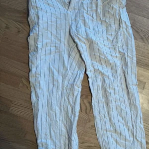 Randiga vita linnebyxor - Snygga vita linnebyxor med tunna vertikala svarta ränder. Byxorna har en avslappnad passform och är perfekta för varma dagar. Lätta och luftiga, passar grymt till sneakers eller sandaler.