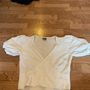 Vit omlottopp från Gina Tricot XS - Supersöt vit omlottopp från Gina Tricot i storlek XS. Toppen har puffiga korta ärmar och djup v-ringning. Tillverkad i mjuk bomull, perfekt för en fräsch och trendig look. Enkel att matcha med både jeans och kjol.
