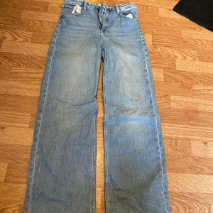 Blå wide jeans från H&M, hög midja - Säljer ett par ljusblå jeans från H&M med wide fit och hög midja. Jeansen har justerbar midja och klassisk femficksdesign. Perfekta för dig som gillar en avslappnad och trendig look.