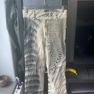Y2k mönstrade byxor  - Storlek L men passar S/M!!Unika byxor i beige och svart med ett coolt abstrakt mönster som påminner om djurprint. Byxorna har raka ben, hög midja och dubbla knappar i midjan. Tillverkade i ett mjukt, lätt material som känns skönt mot huden. 