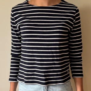 Randig långärmad tröja  - Snygg långärmad tröja med marinblå och vita horisontella ränder. Tröjan har en rak passform och är tillverkad i mjuk bomull, perfekt för en avslappnad och stilren look. Passar lika bra till jeans som till kjol.