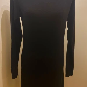 Svart stickad långärmad klänning Esmara 38/40 - En svart, stickad klänning med lång ärm och rund halsringning. Klänningen har en snygg dragkedja i guld baktill som detalj och är figurnära i modellen. Perfekt för dig som gillar en enkel men stilren look.