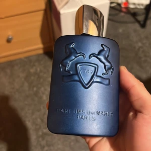 Layton Eau de Parfum från Parfums de Marly - Exklusiv parfymflaska i matt mörkblått med silverfärgad kork och upphöjt emblem med två hästar. Layton är en lyxig doft från Parfums de Marly, Paris. Flaskan rymmer 125 ml och är tillverkad i Frankrike. 
