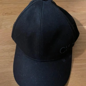 Svart keps från Calvin Klein - Snygg svart keps från Calvin Klein med broderad CK-logga framtill. Kepsen har en justerbar rem baktill med en metallspänne för perfekt passform. Perfekt för en stilren look.