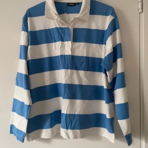 Blåvit randig pikétröja från KappAhl - Använd 3-4 gåner. En blåvit randig pikétröja från KappAhl. Tröjan har långa ärmar och en klassisk krage. Perfekt för en avslappnad stil. Hör av dig vid intresse!