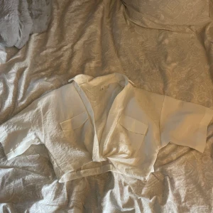 Vit croppad blus - Säljer en stilren vit croppad blus med korta ärmar och två bröstfickor. Perfekt för en avslappnad look. Passar bra till jeans eller kjol.