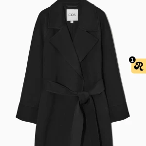 Svart kappa från COS - Elegant svart kappa från COS med klassisk design och knytskärp i midjan. Perfekt för en stilren look under kyligare dagar. Kappan har långa ärmar och en tidlös siluett.