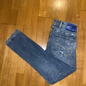 Blå jeans från Jack & Jones - Snygga blå jeans från Jack & Jones med slitna detaljer och en klassisk femficksdesign. Jeansen har en knappgylf och är perfekta för en avslappnad stil. De har en normal passform och är tillverkade i ett slitstarkt denimtyg. Priset kan möjligen sänkas vid en snabb affär!