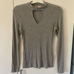 Tight Hollister - Säljer en stilren tight tröja från Hollister. Tyget är mjukt och följsamt. Tröjan har en unik öppning med v-ringad design med en vid halsen och långa ärmar. Passar till många olika stilar och tillfällen.