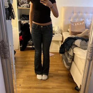 Intressekoll - Säljer ett par mörkblå bootcut jeans med låg midja. Jeansen har dekorativa sömmar på bakfickorna och en klassisk femficksdesign. Perfekta för en avslappnad stil.