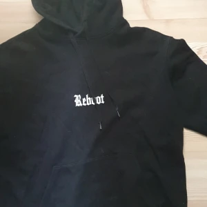Svart hoodie från William Baxter - Säljer en svart hoodie från William Baxter med texten 'Reboot' på bröstet. Den har en klassisk design med huva och dragsko samt en stor magficka framtill. Perfekt för en avslappnad stil.