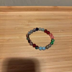 Färgglatt armband med pärlor - Säljer ett färgglatt armband med pärlor i olika nyanser av blått, rött, grönt och rosa. Armbandet är elastiskt och passar de flesta handleder. Perfekt för att lägga till en färgklick till din outfit!